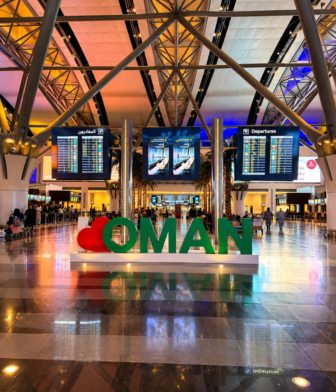 Umman’daki havalimanı terminalinde Oman yazısı, kalkış bilgi ekranları ve yolcuların yer aldığı modern terminal alanı